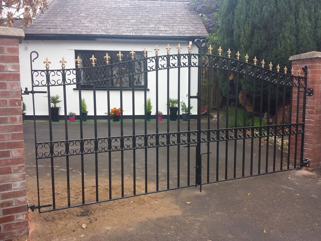 Wrought iron driveway gates with gold-tipped fleur-de-lis finials and scrollwork