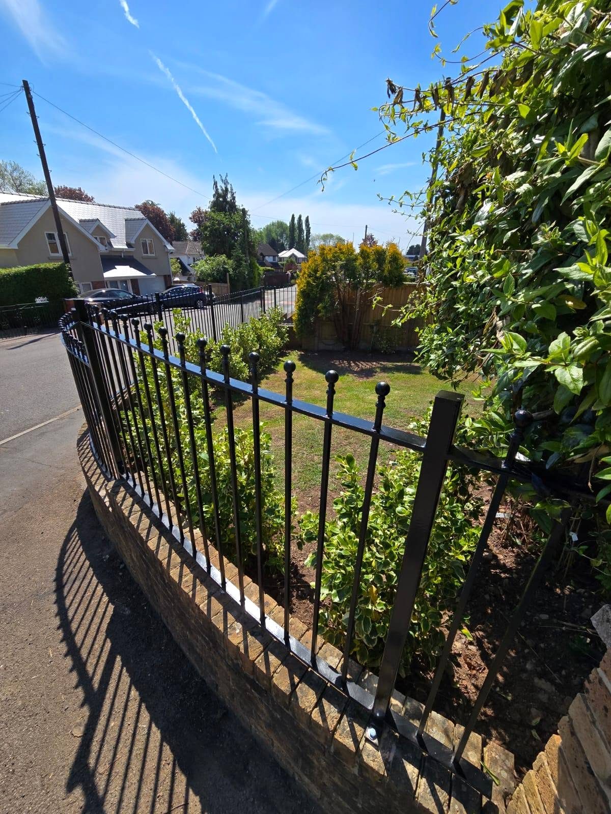 Black ball-top railings curving along a garden boundary wall