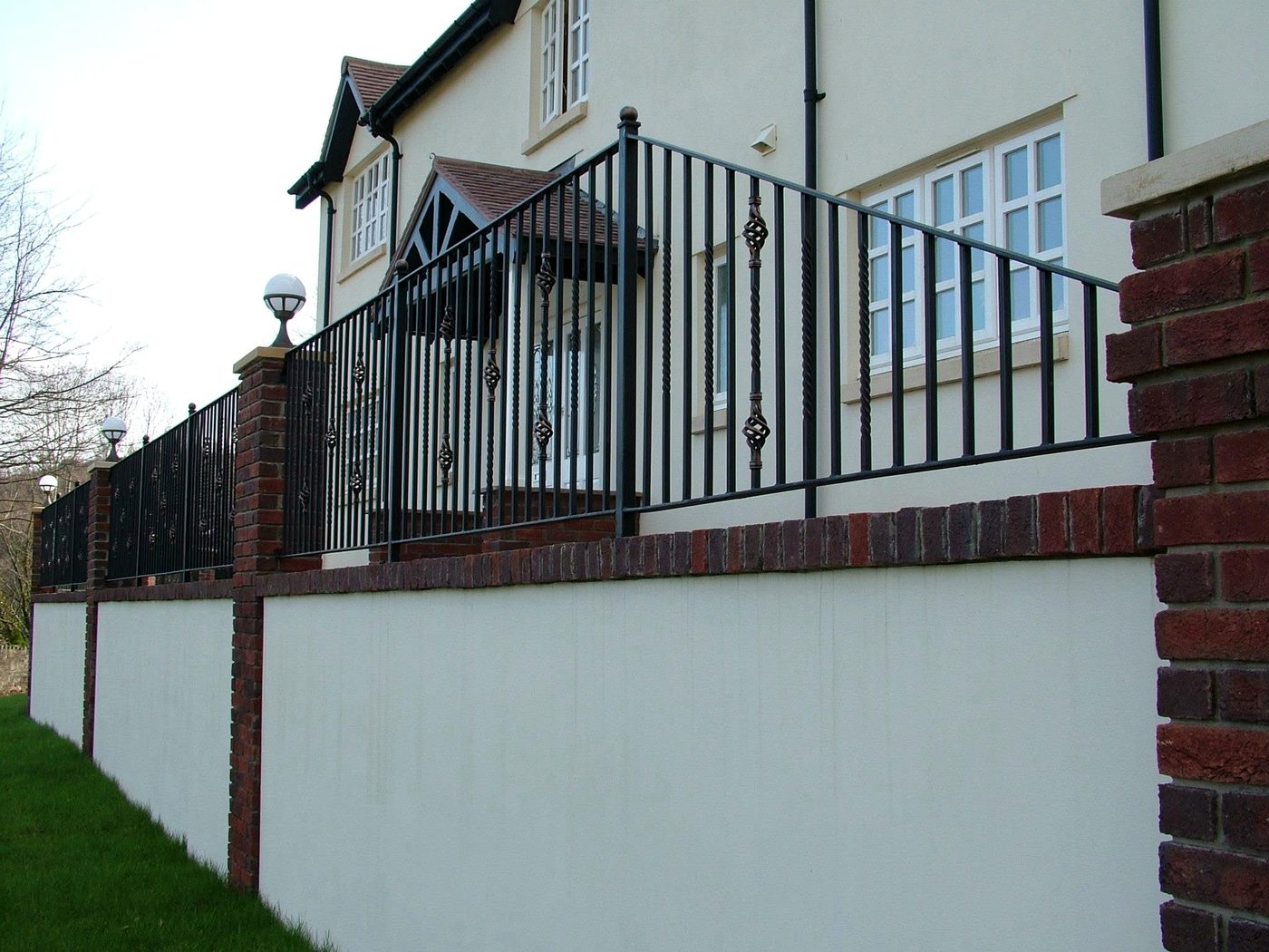 Black railings with cage-twist balusters mounted on a rendered boundary wall