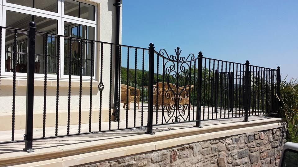 Wrought iron terrace railings with a central decorative scroll panel and cage-twist balusters