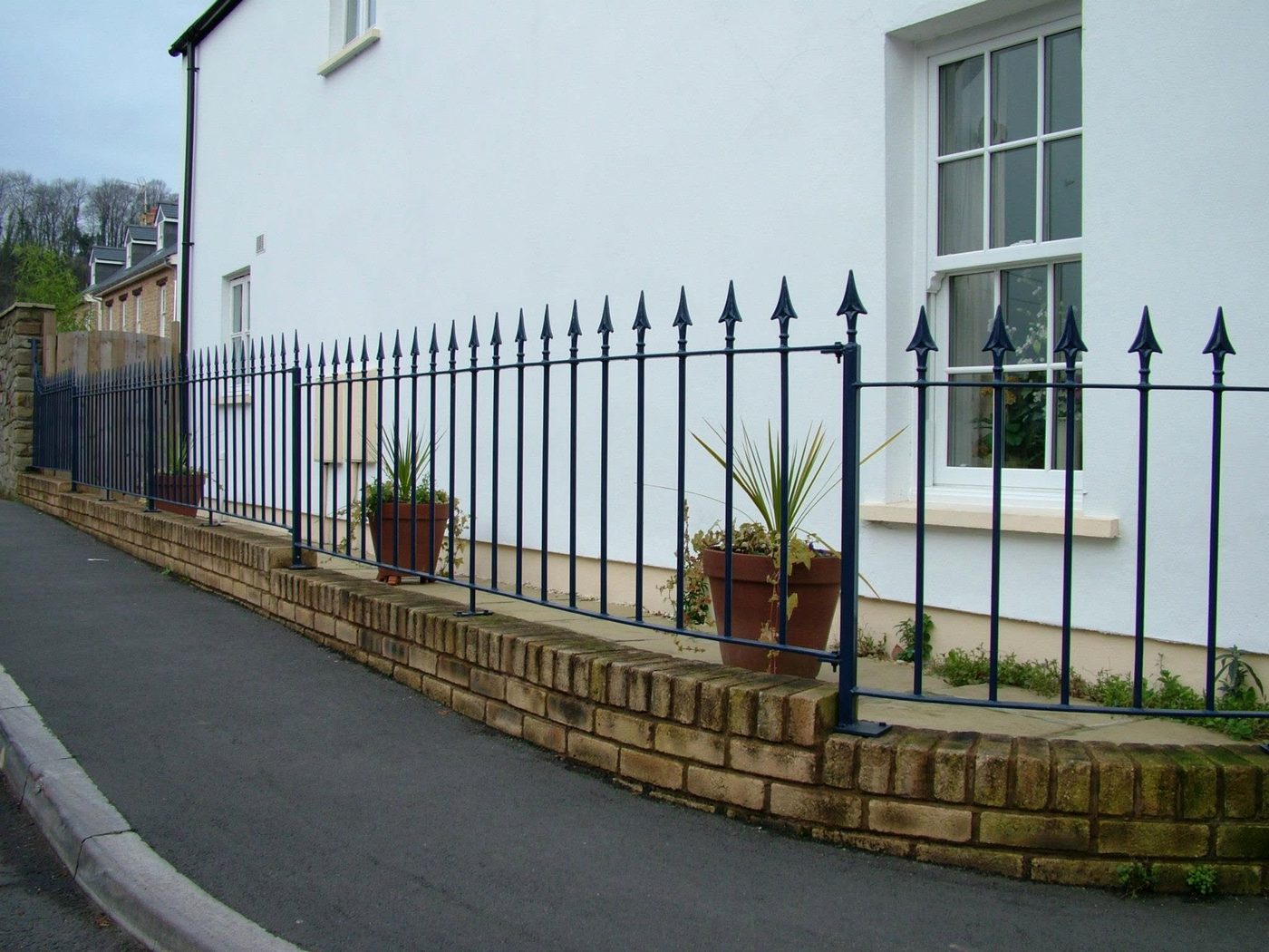 Blue-black spear-top wrought iron railings on a low stone wall beside a cottage